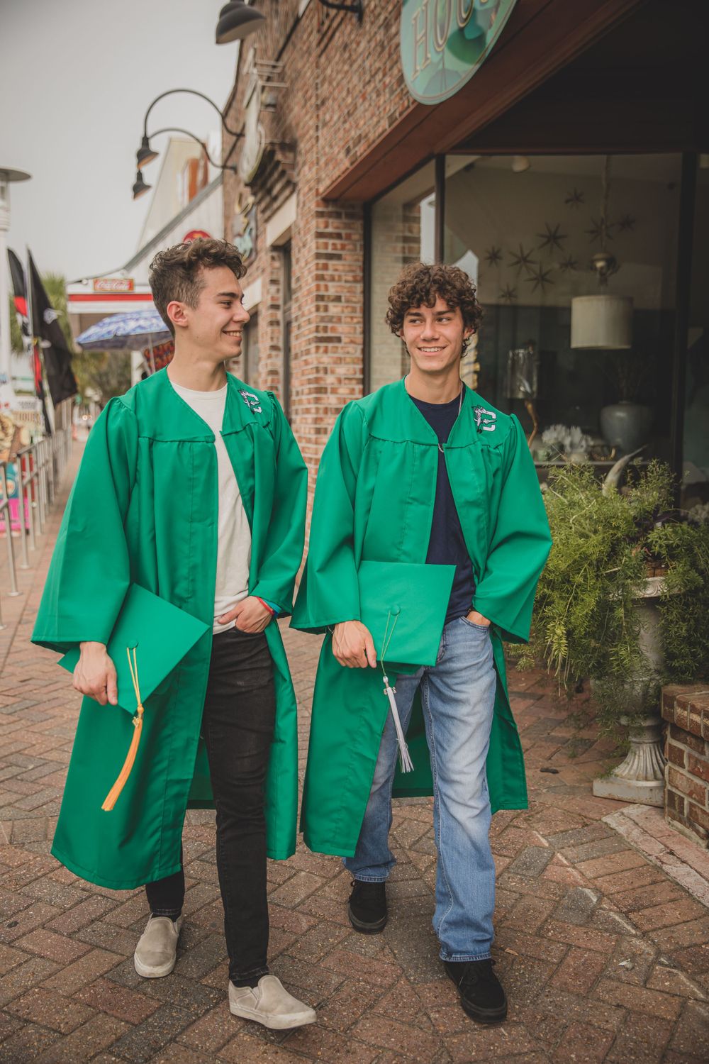 Two graduates in bright green graduation gowns walk along a brick-paved street.