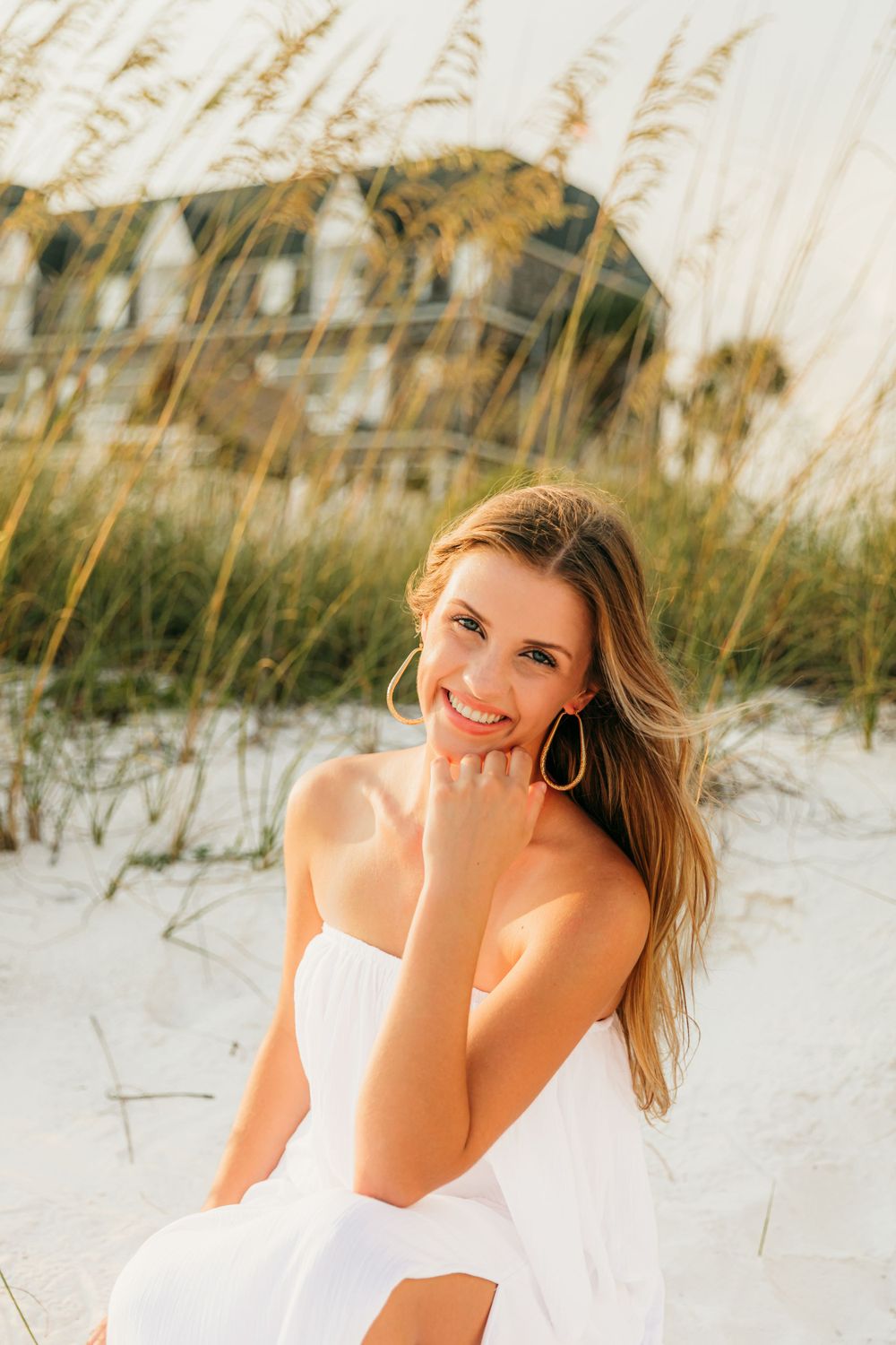 Person in white dress sitting on beach with sea oats at sunset.