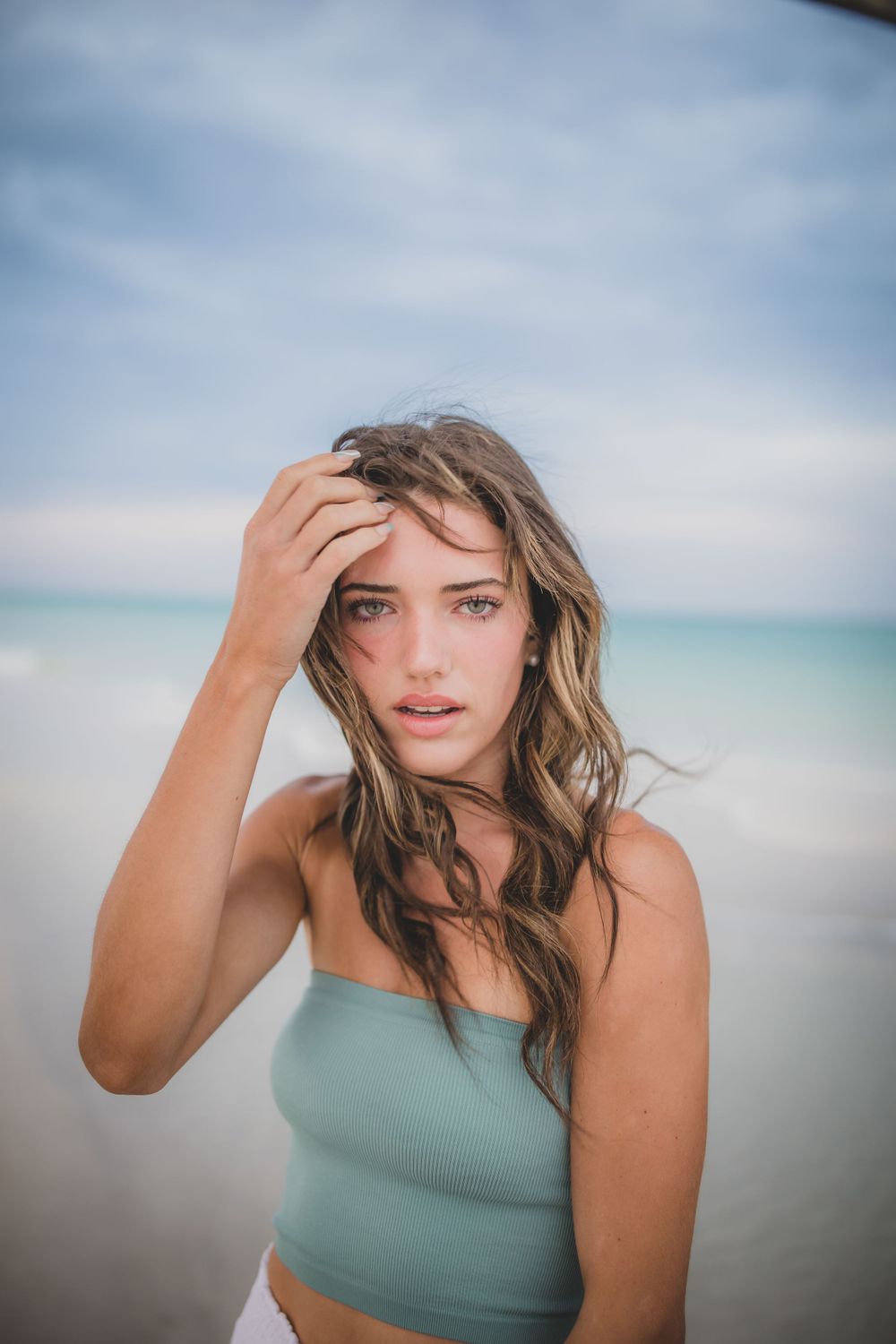 Person in teal crop top with windswept hair against ocean background.