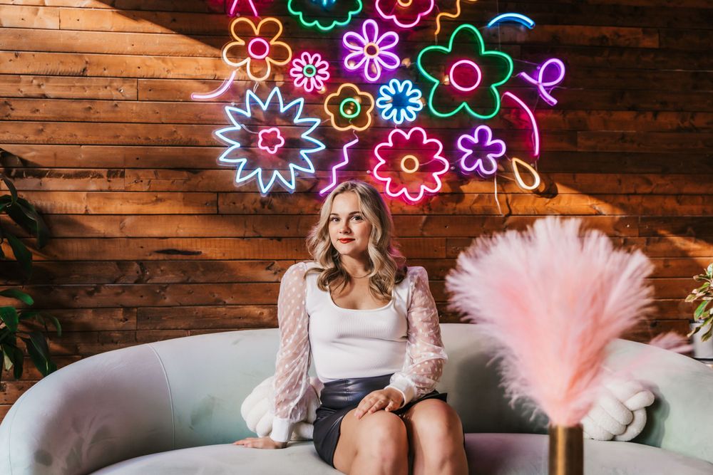 Indoor portrait session with colorful neon flower lights creating a vibrant backdrop against wooden walls.
