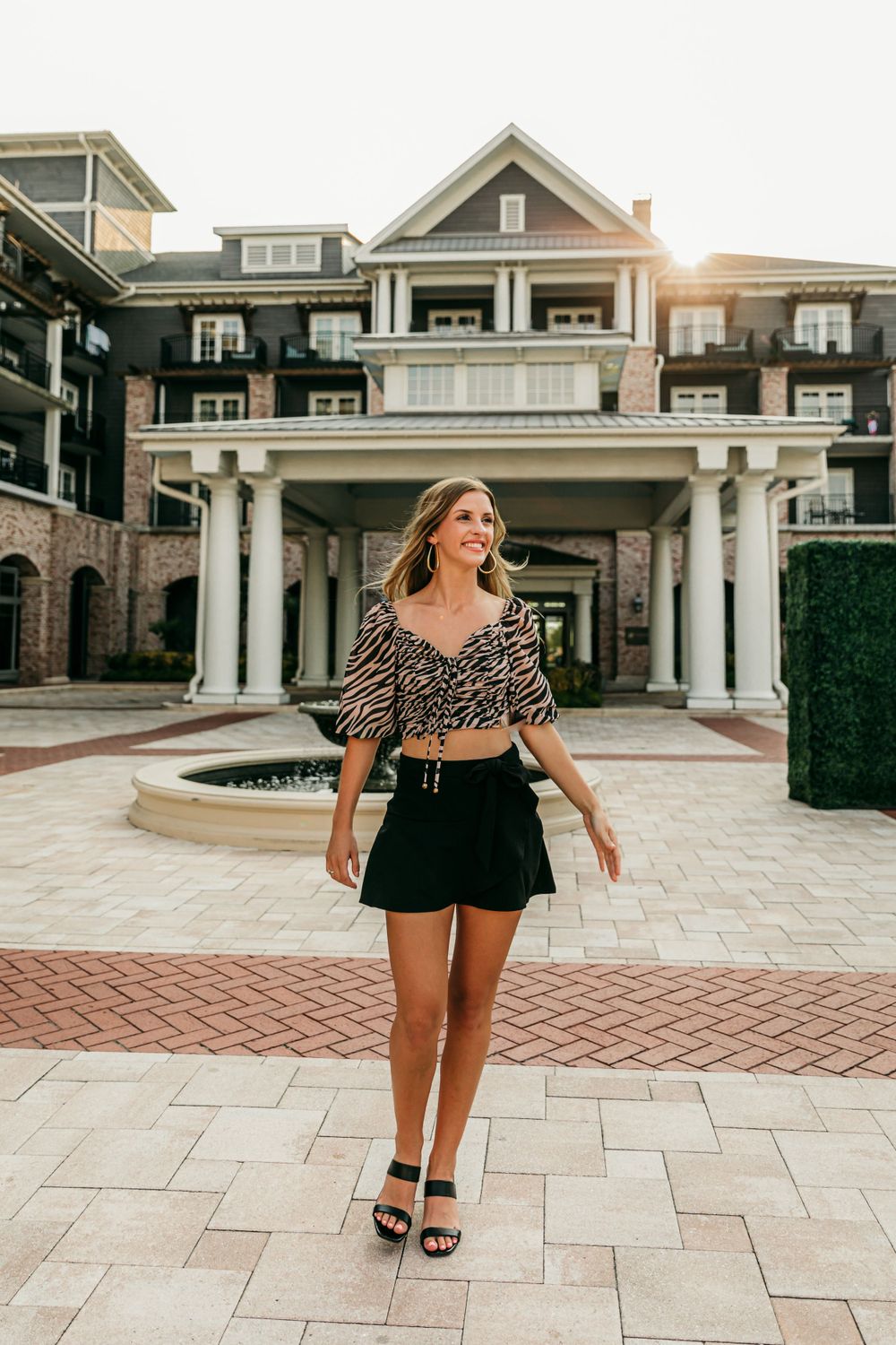 Person in animal print top and black shorts walking in front of luxury resort building.