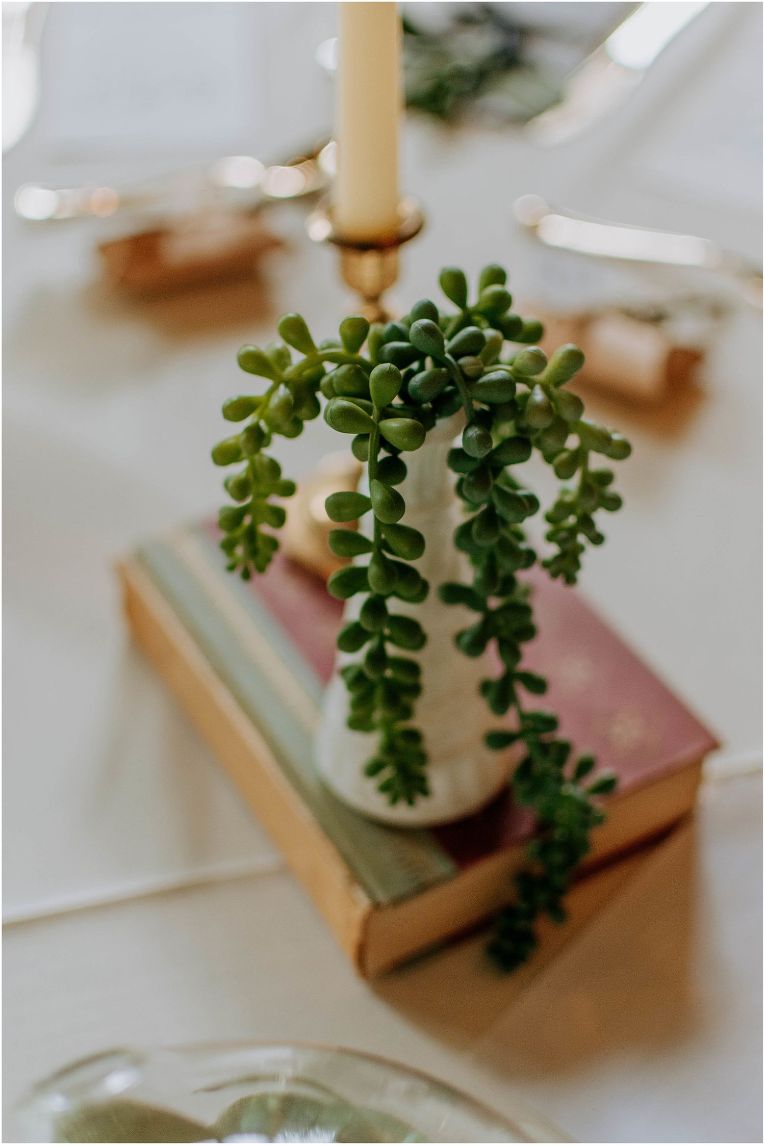 Delicate succulent centerpiece arrangement in white vase atop stacked vintage books on table.