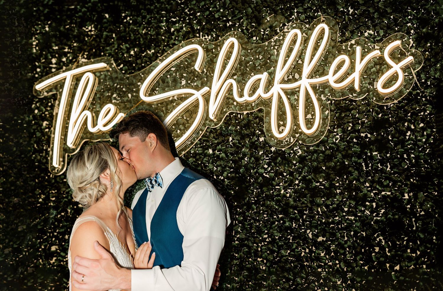 A romantic wedding portrait with a couple kissing under illuminated custom signage.