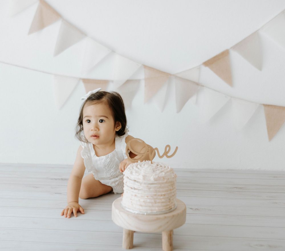 White minimalist cake smash setup with bunting decorations against light backdrop.