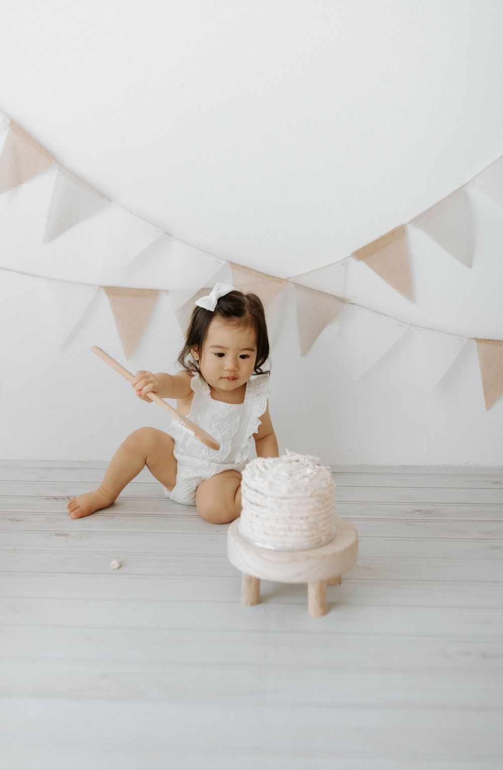 Small child reaching toward white cake on wooden stand with festive bunting backdrop.