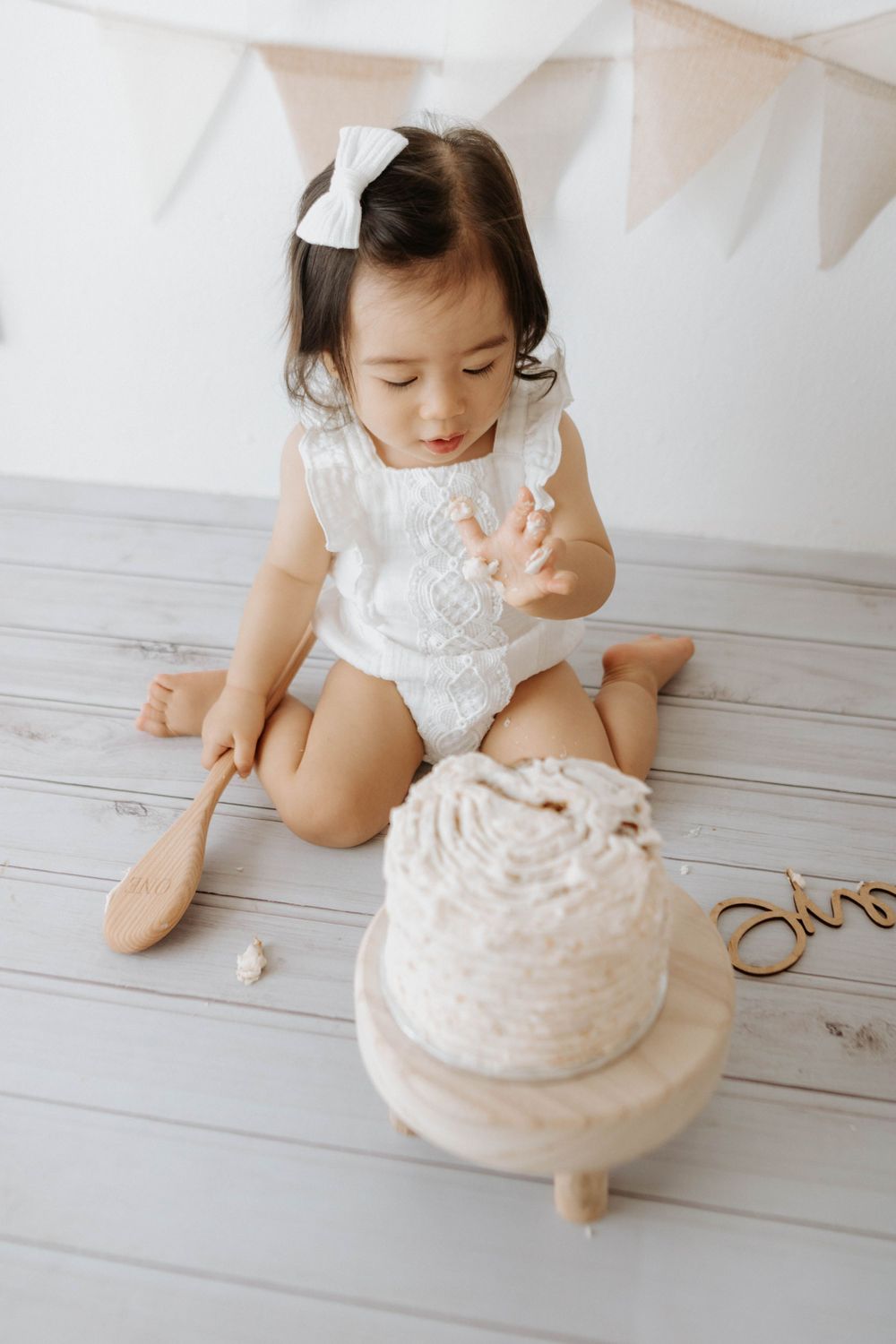 Baby exploring and tasting white frosted cake during cake smash photo session.