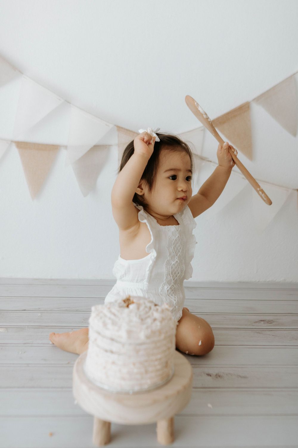 A small child holds up wooden spoons during cake smash photoshoot with party decorations.