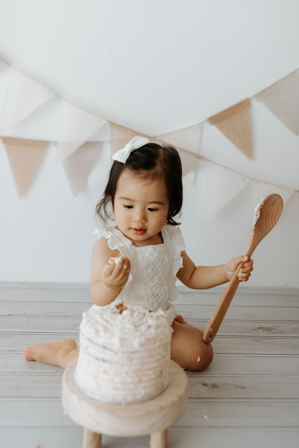 A white cake smash photo setup with bunting decorations and a small wooden spoon.