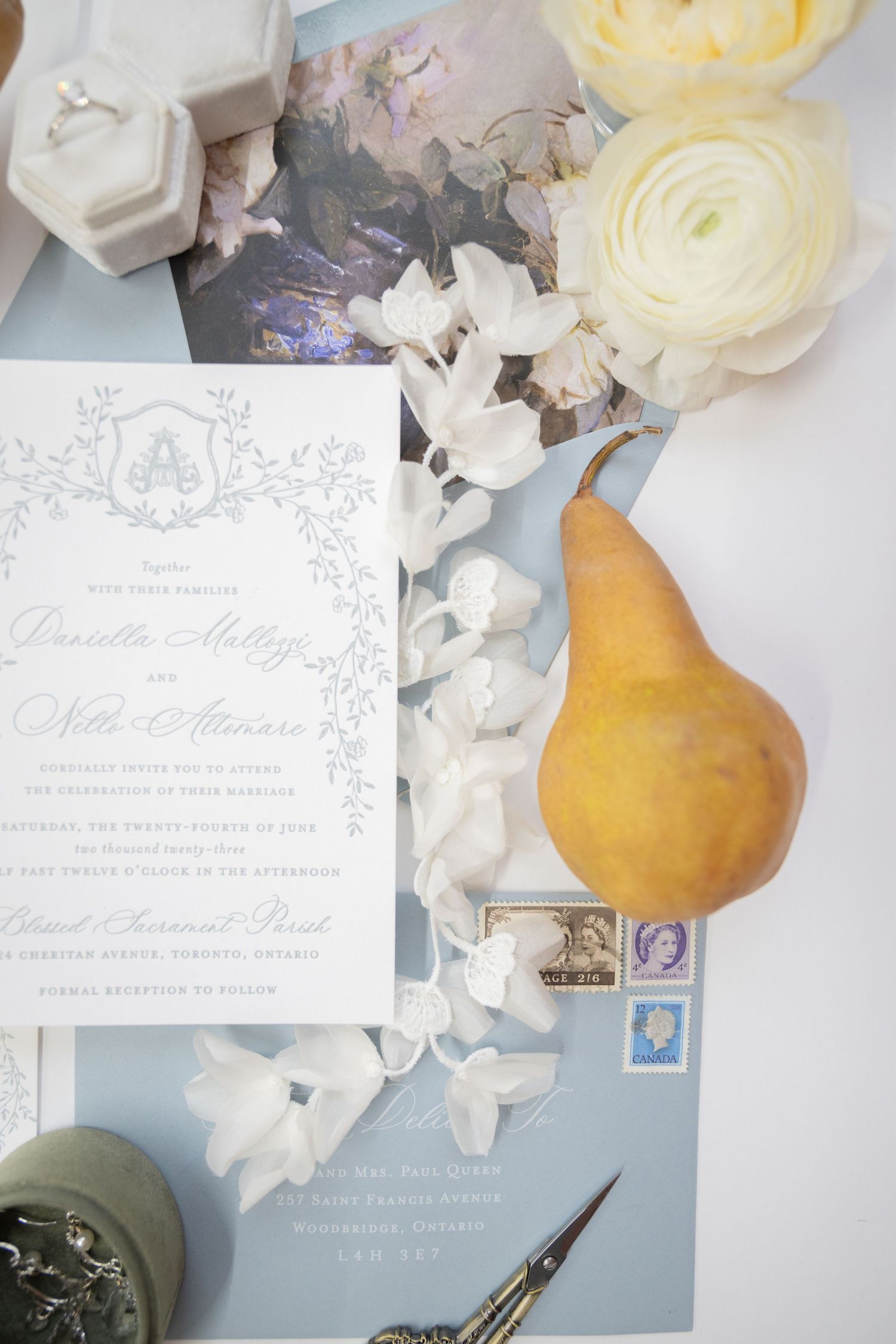 Elegant wedding invitation with cream roses, vintage stamps, and a golden pear on light blue background.