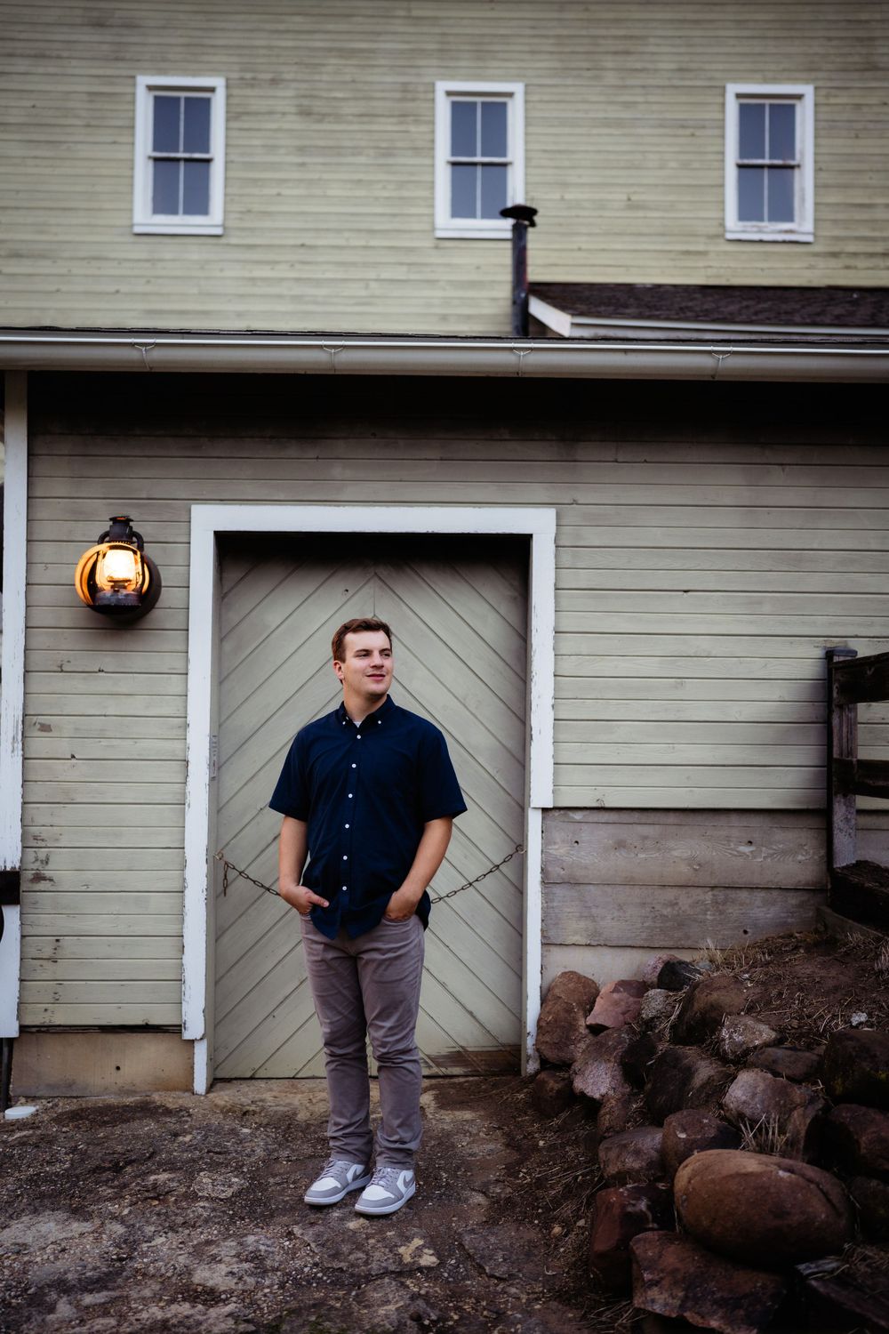 Person standing in front of vintage beige house with diagonal door pattern and rustic lantern.