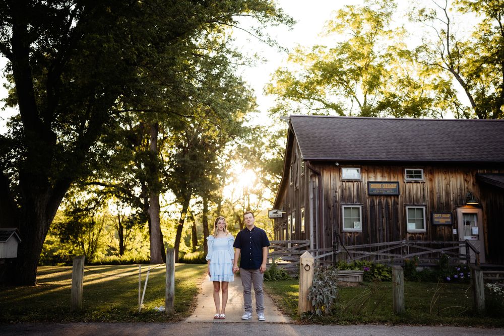 Couple walking hand in hand on path near rustic barn during golden hour.