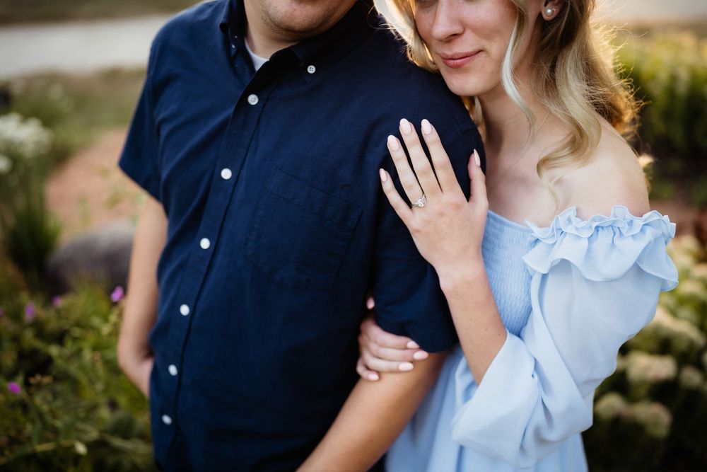 Close-up of couple in blue attire showing engagement ring outdoors.