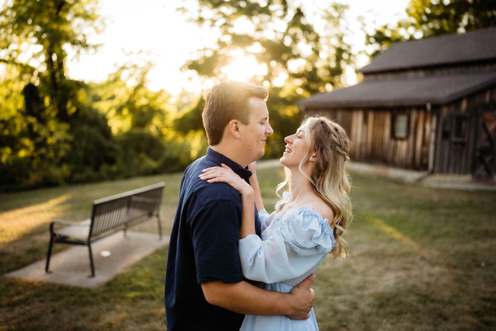 Couple sharing intimate moment in golden sunlight near rustic barn setting.