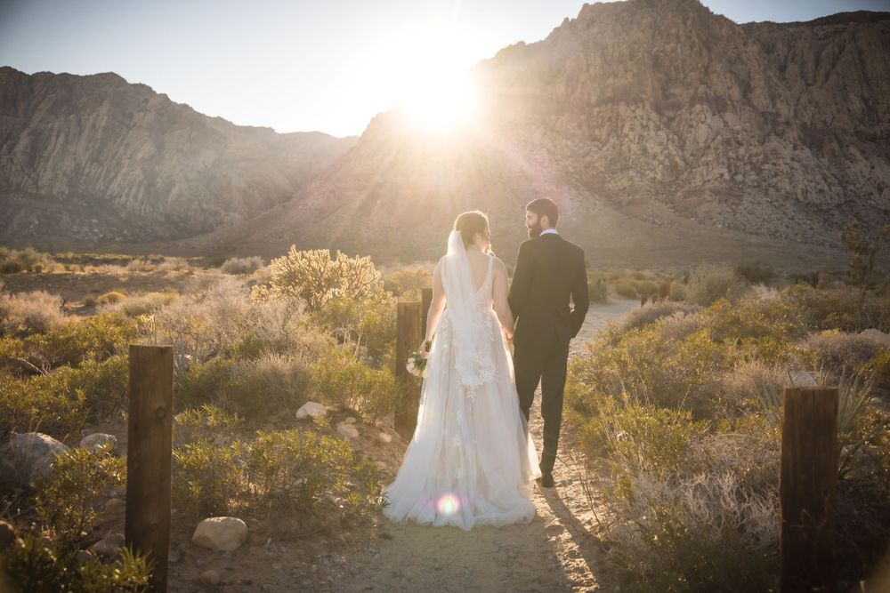 A silhouette of a wedding couple against a golden sunset in a desert mountain landscape.
