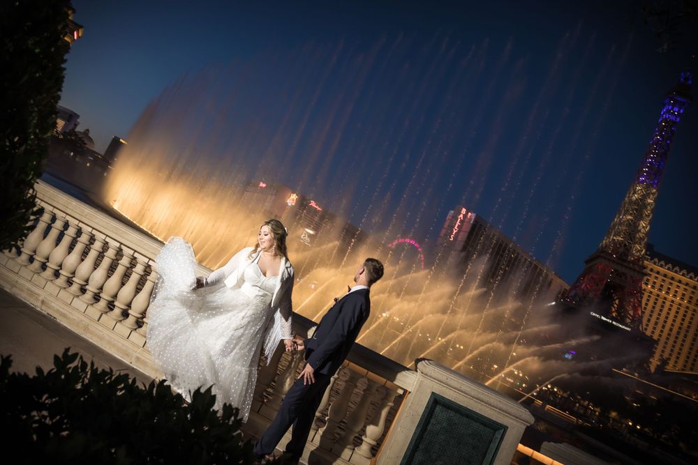 A dramatic nighttime wedding photo with illuminated fountains and city lights in the background.