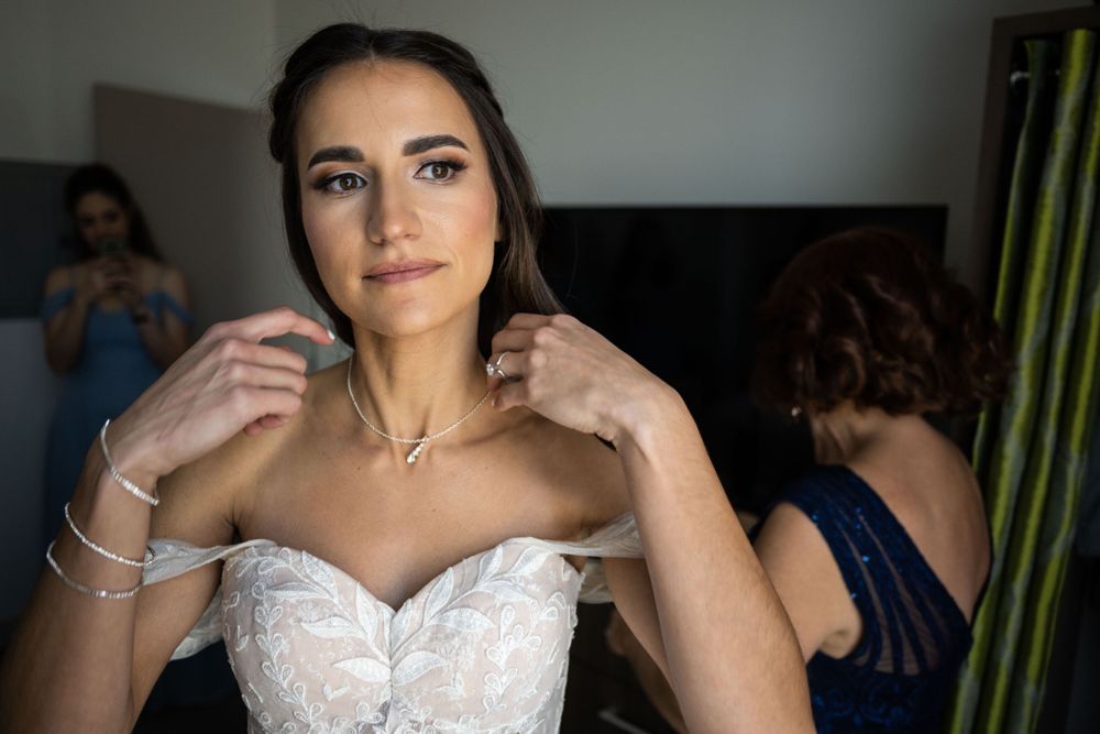 A bride adjusts her jewelry while wearing a strapless white wedding gown.