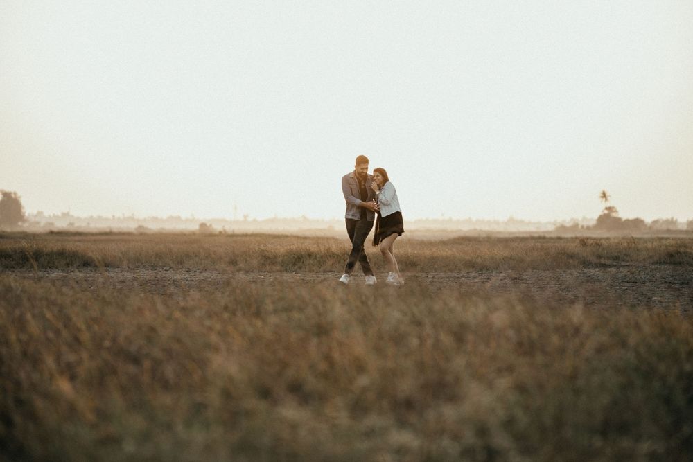 Distant view of couple sharing intimate moment in open field at dusk.