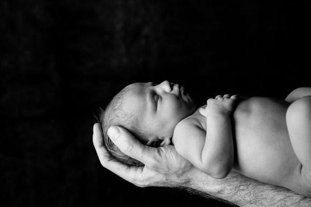 Black and white portrait of sleeping newborn baby supported by gentle hands.