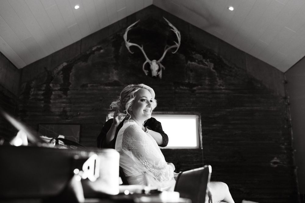 Black and white bridal portrait in rustic cabin setting with mounted deer antlers on wall.