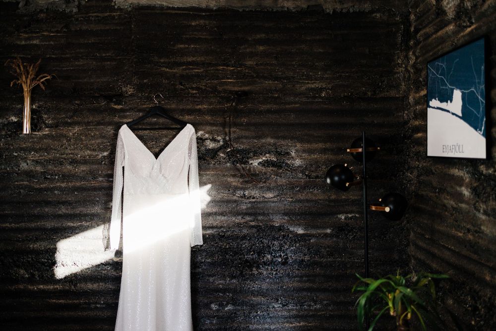 White wedding dress hanging against a dark rustic wooden wall with dramatic lighting.