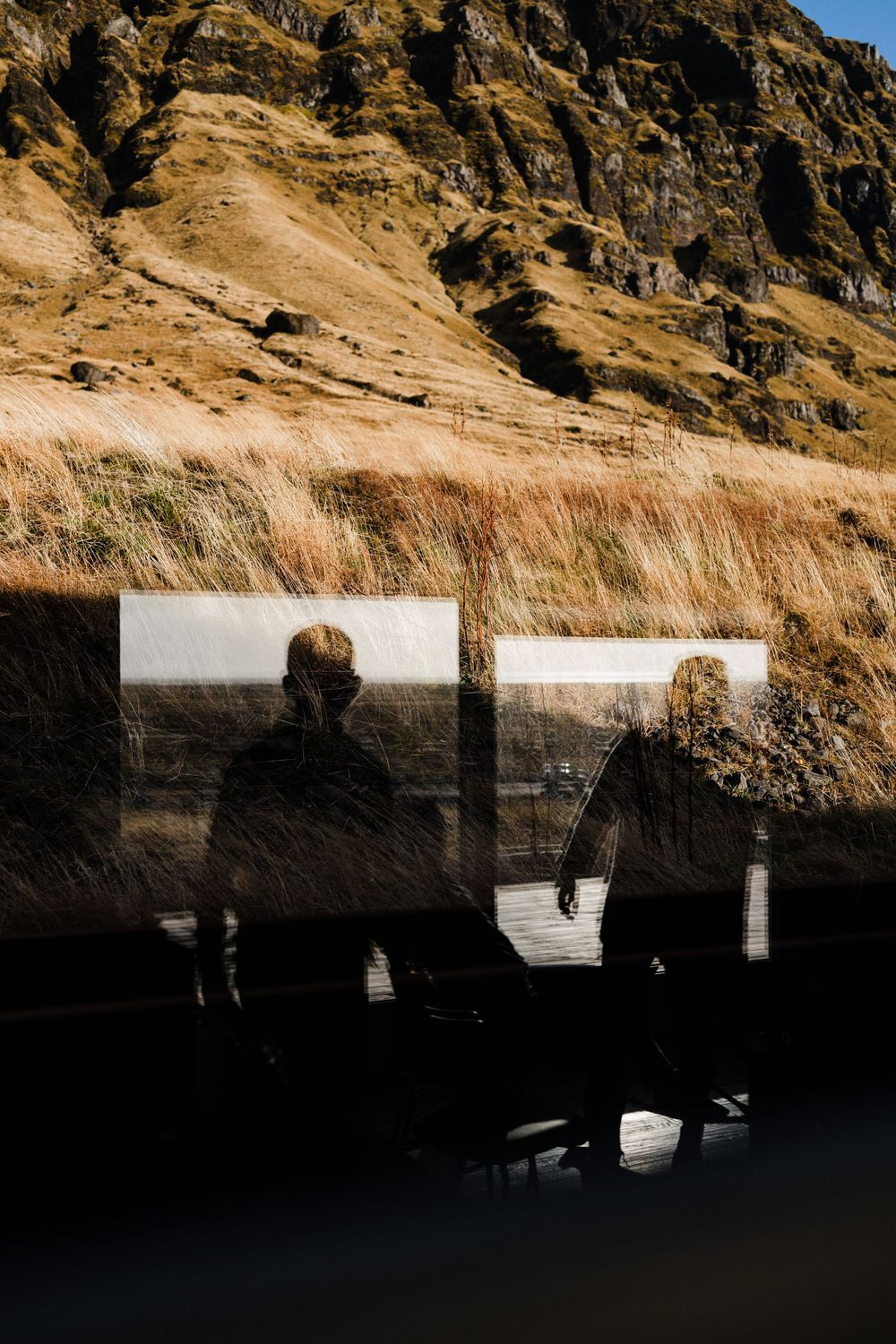 Dramatic mountain landscape with silhouettes reflected in window glass.