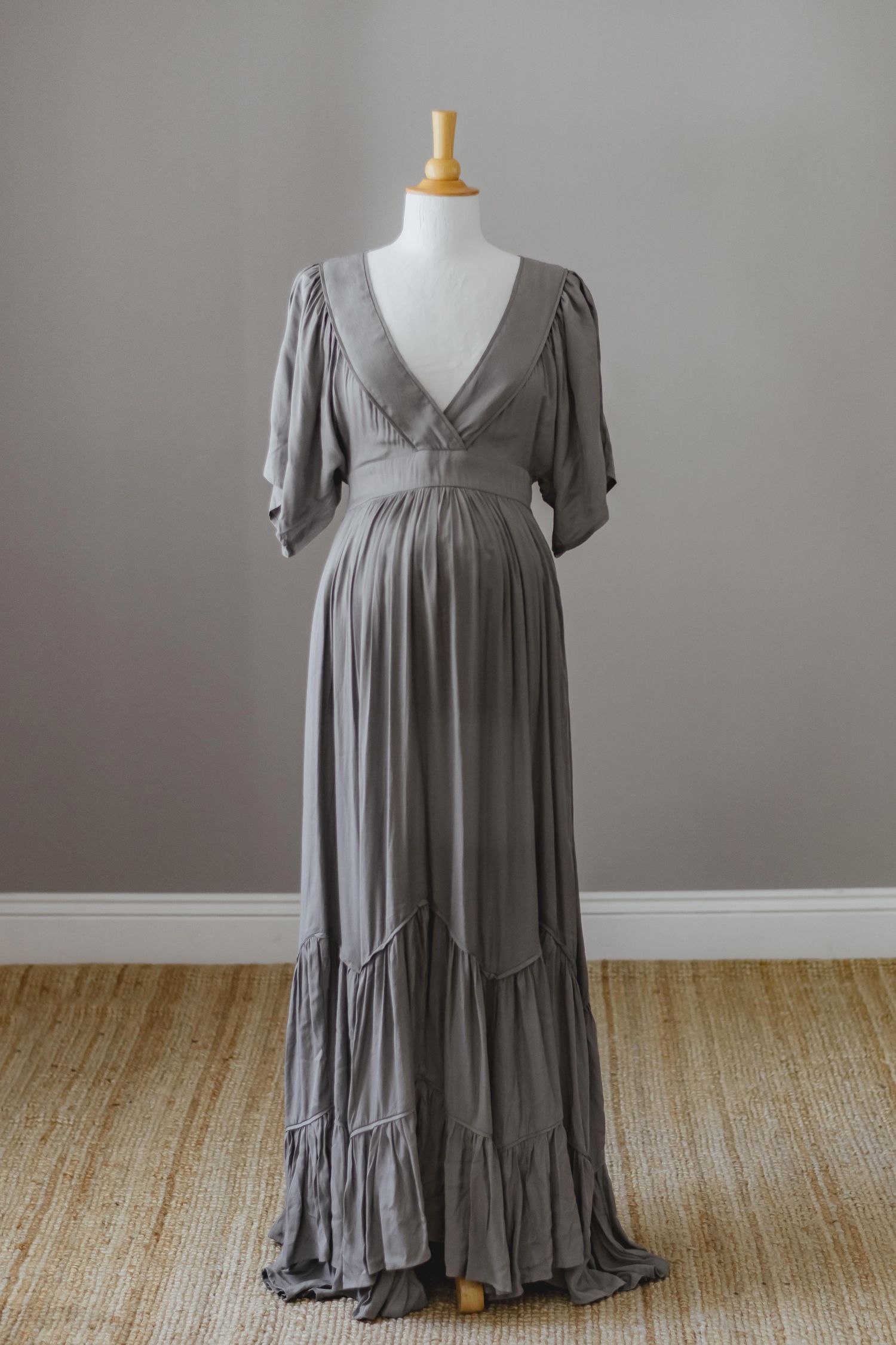 Long grey maternity dress with empire waist and tiered skirt on mannequin.