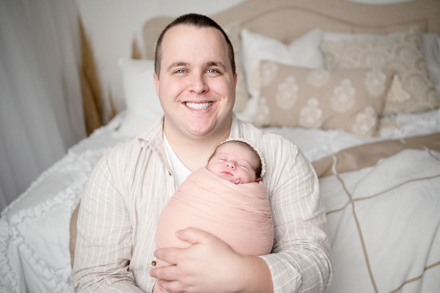 Parent in white sweater holding newborn baby wrapped in pink blanket against white bedding.