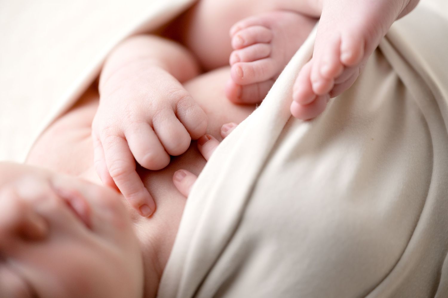 Close-up of tiny baby hands grasping against soft white fabric.