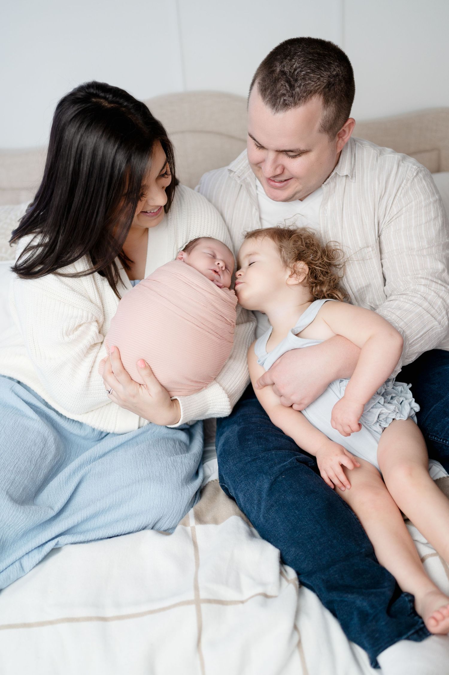 Sweet family moment as toddler kisses newborn sibling while parents watch.