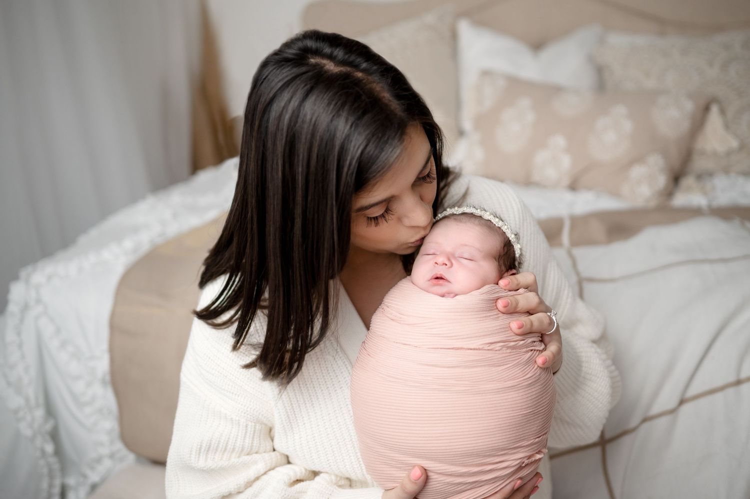 Intimate portrait of mother cradling pink-swaddled newborn against neutral background.