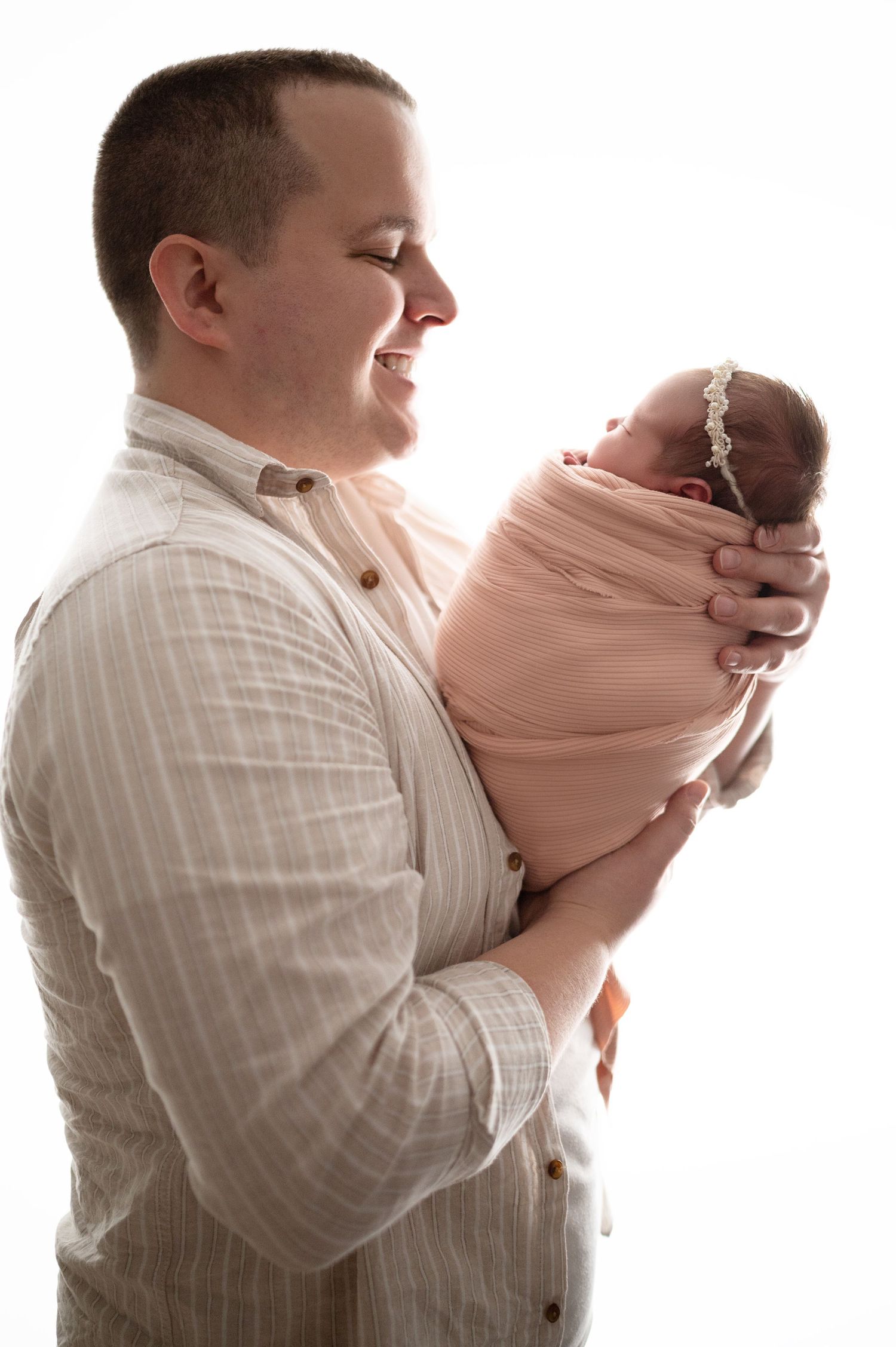 Sequence showing parent cradling newborn in pink wrap against white background.