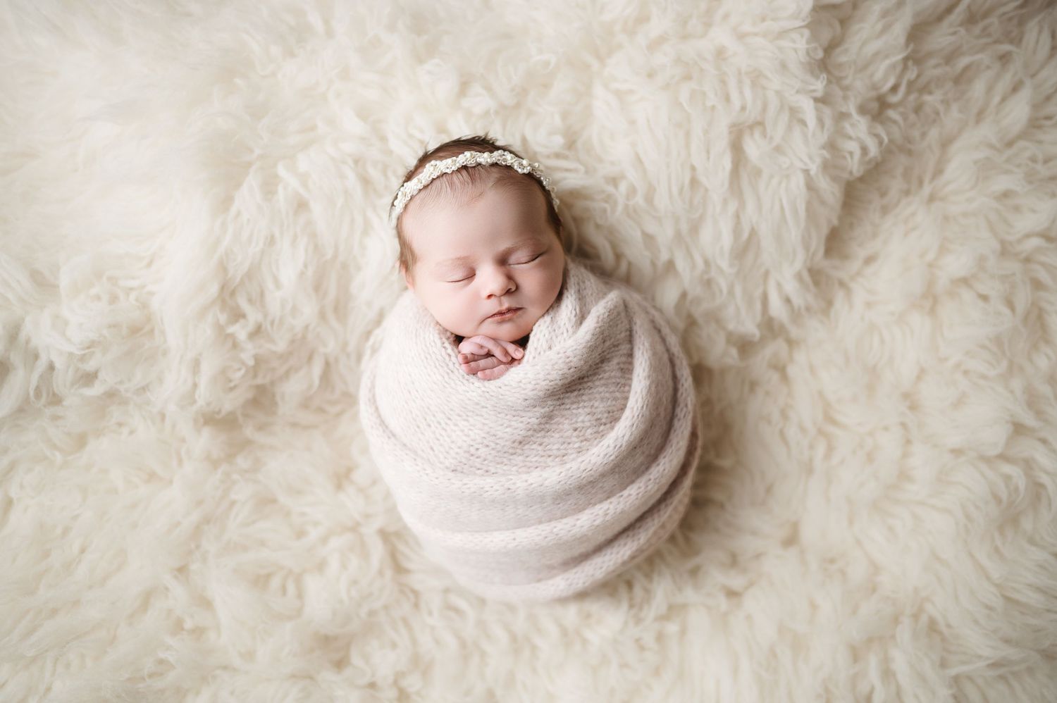 A peacefully sleeping newborn wrapped in soft pink swaddle against white textured background.