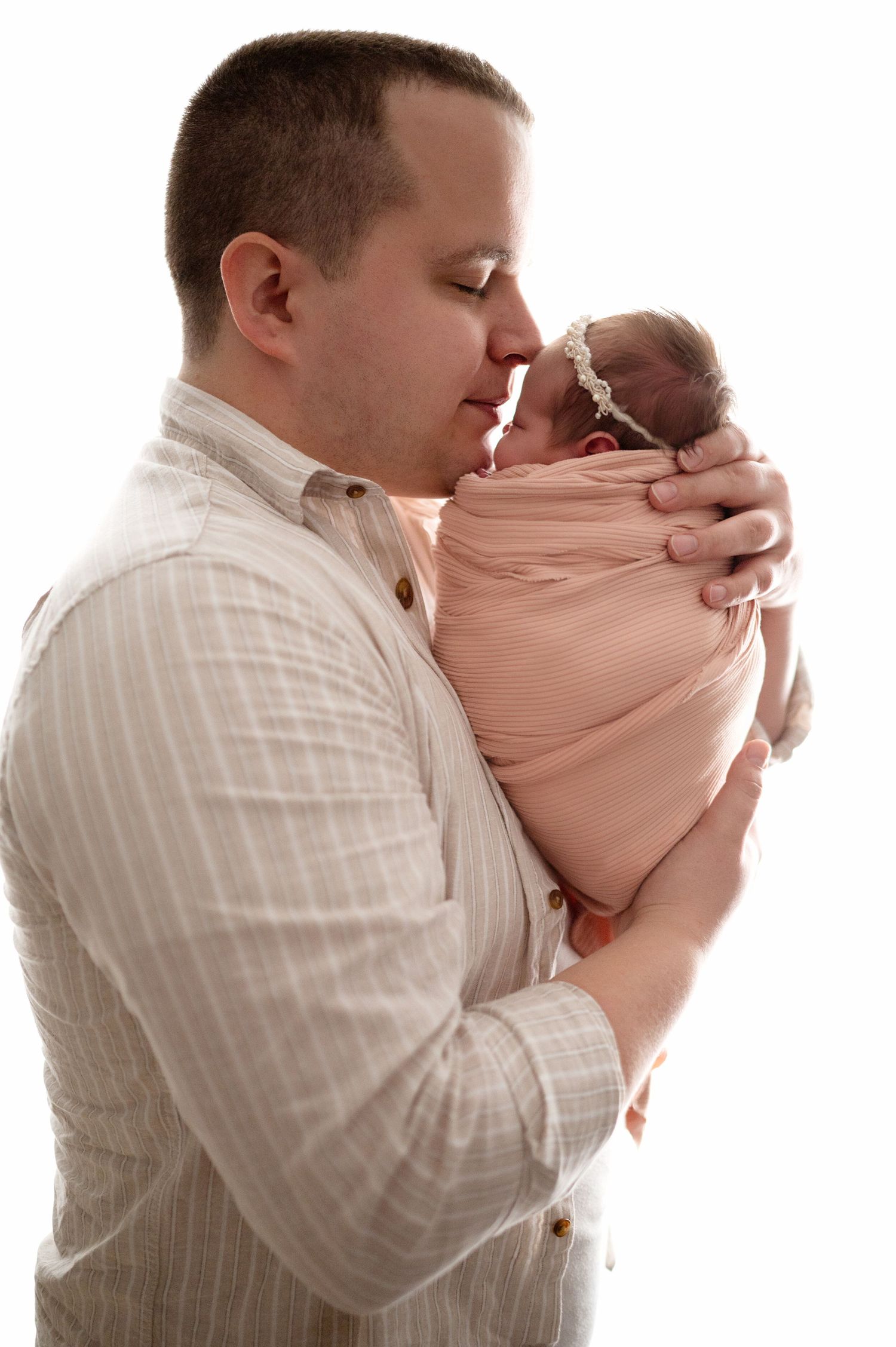 Parent lovingly holding and bonding with swaddled infant in white studio setting.