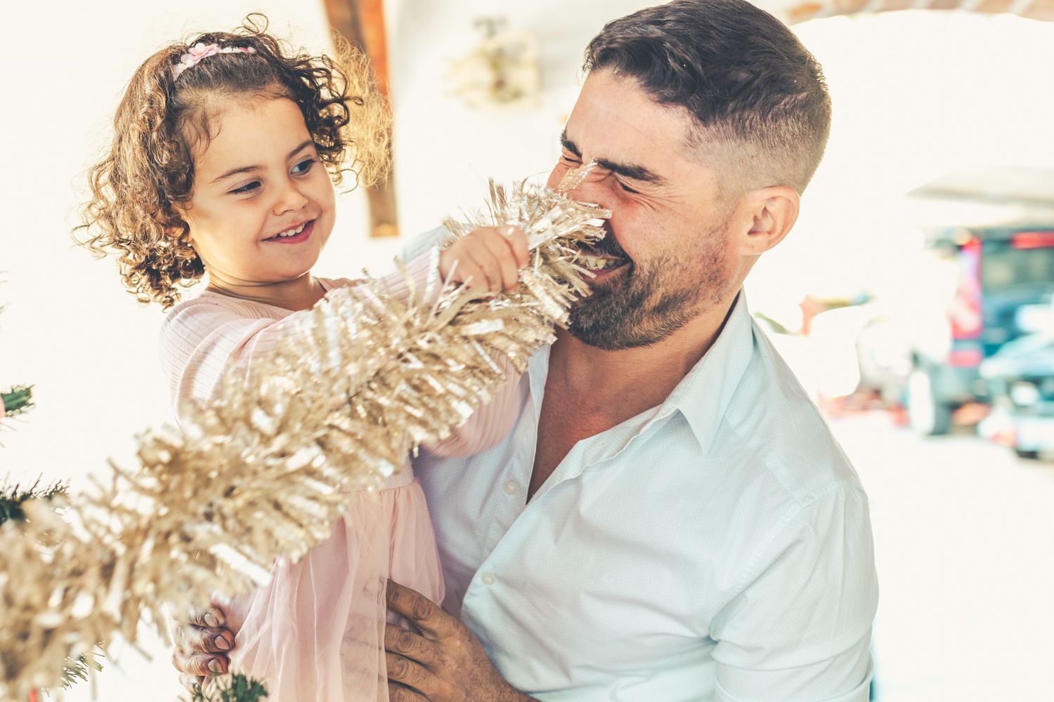 Toddler Lara is making her father laugh with the Christmas silver-colored tinsel.