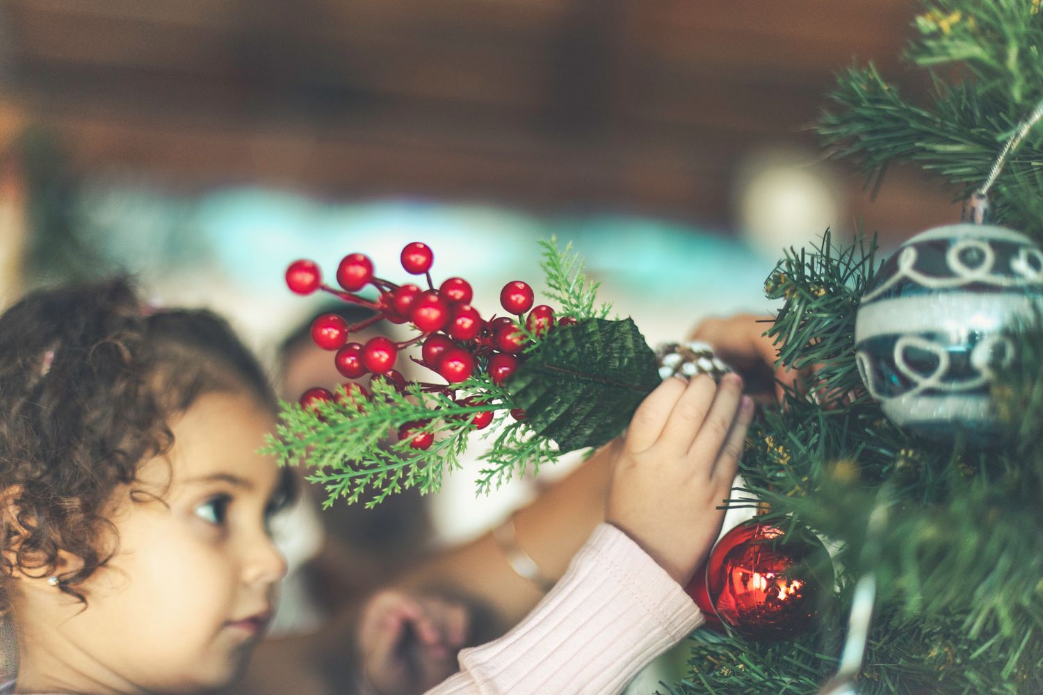Todlerr Lara is decorating the Christmas tree with Christmas berry artificial flowers