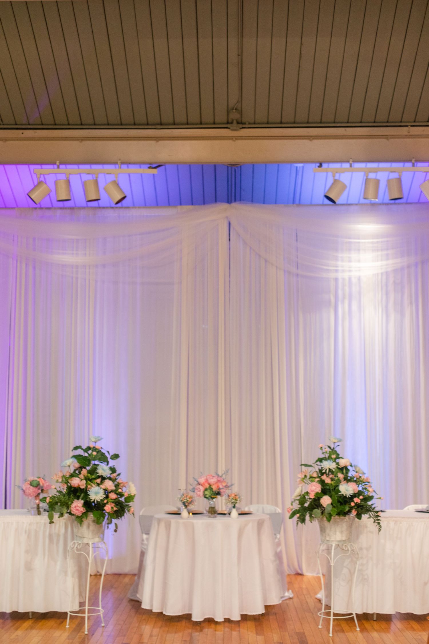 Elegant wedding reception venue with white draping and purple uplighting.