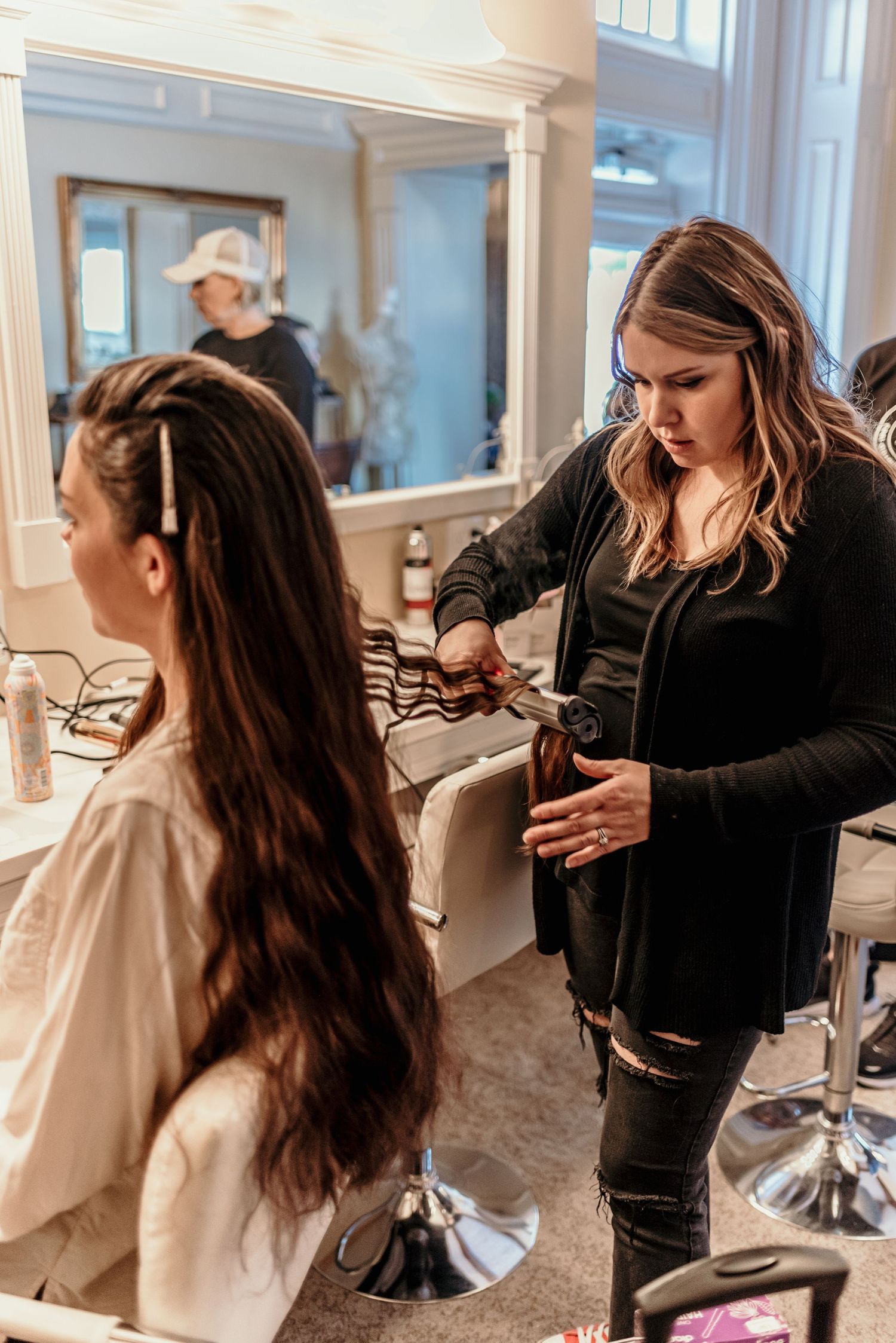 A hairstylist works on styling long dark hair in a salon setting.