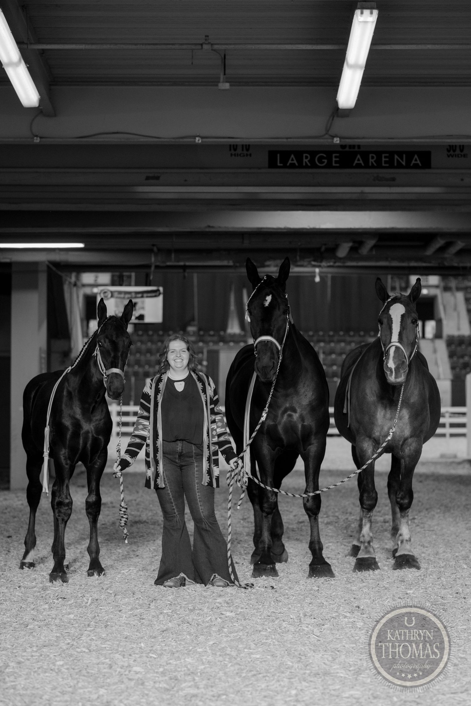 Black and white photo of four horses and handler in indoor equestrian arena.