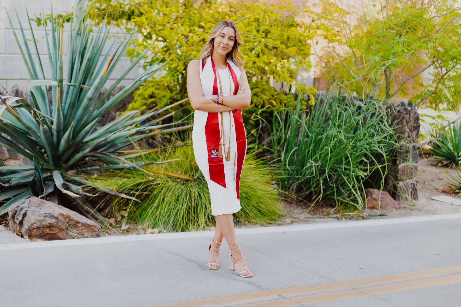 A person in a red dress walks along a desert path with succulents and yellow trees.