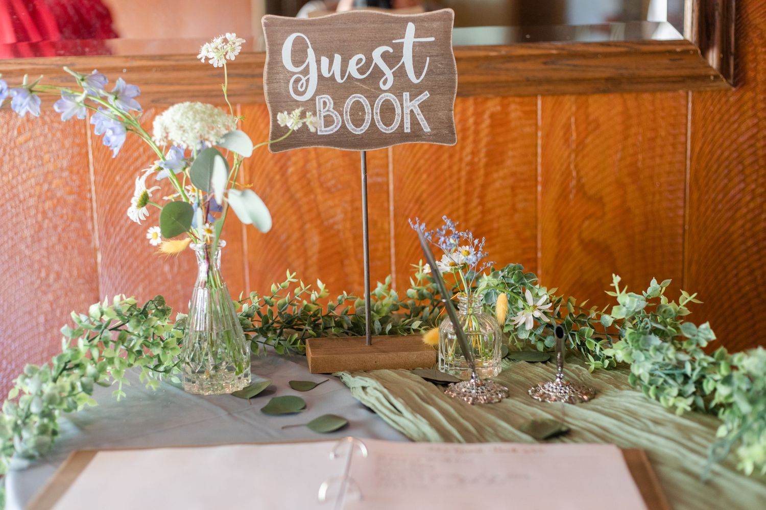 A rustic wedding guest book display with delicate floral arrangements and greenery.