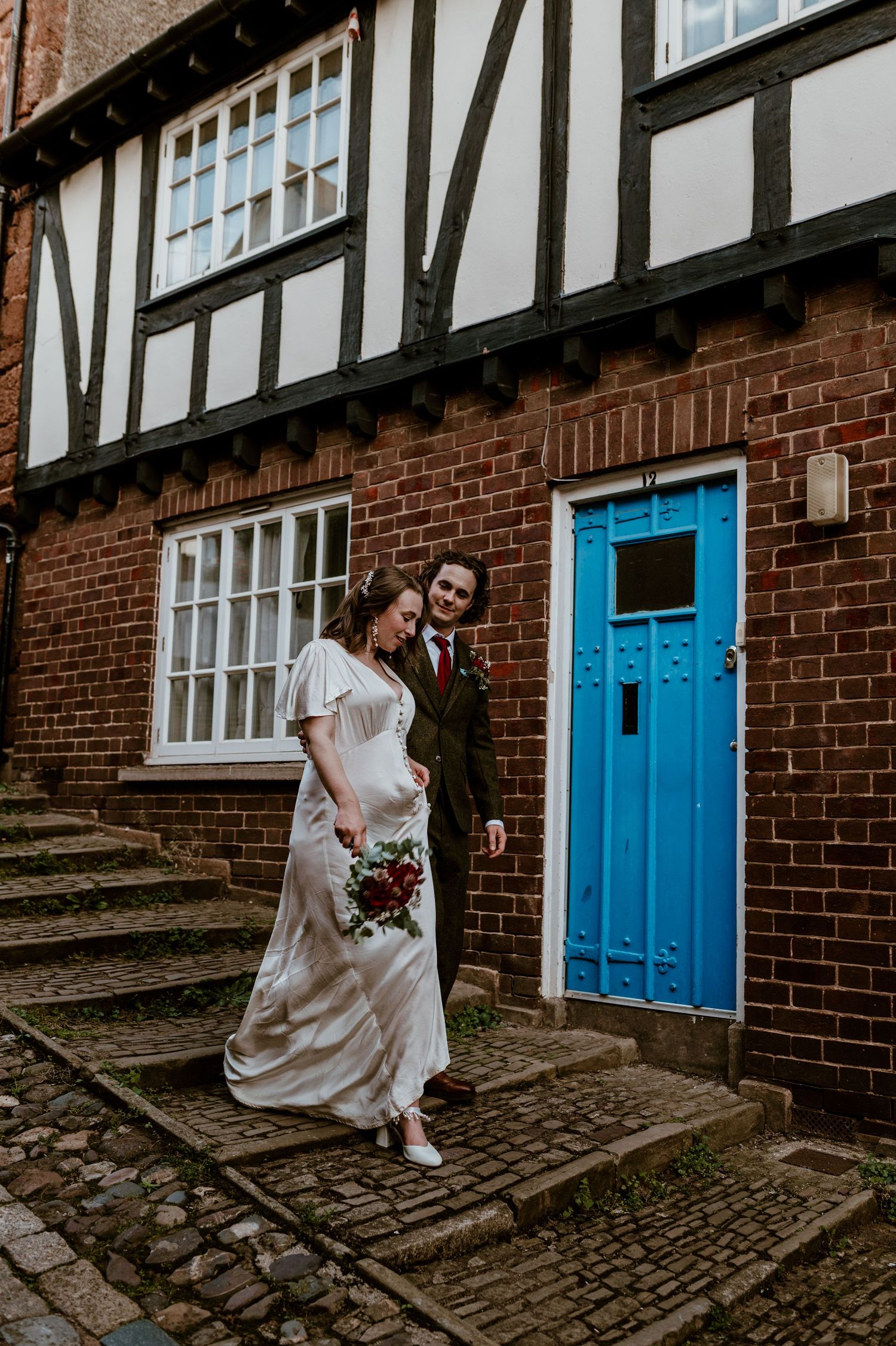 Couple steps outside a charming Tudor-style brick building with half-timbering and a bright blue door in Exeter.