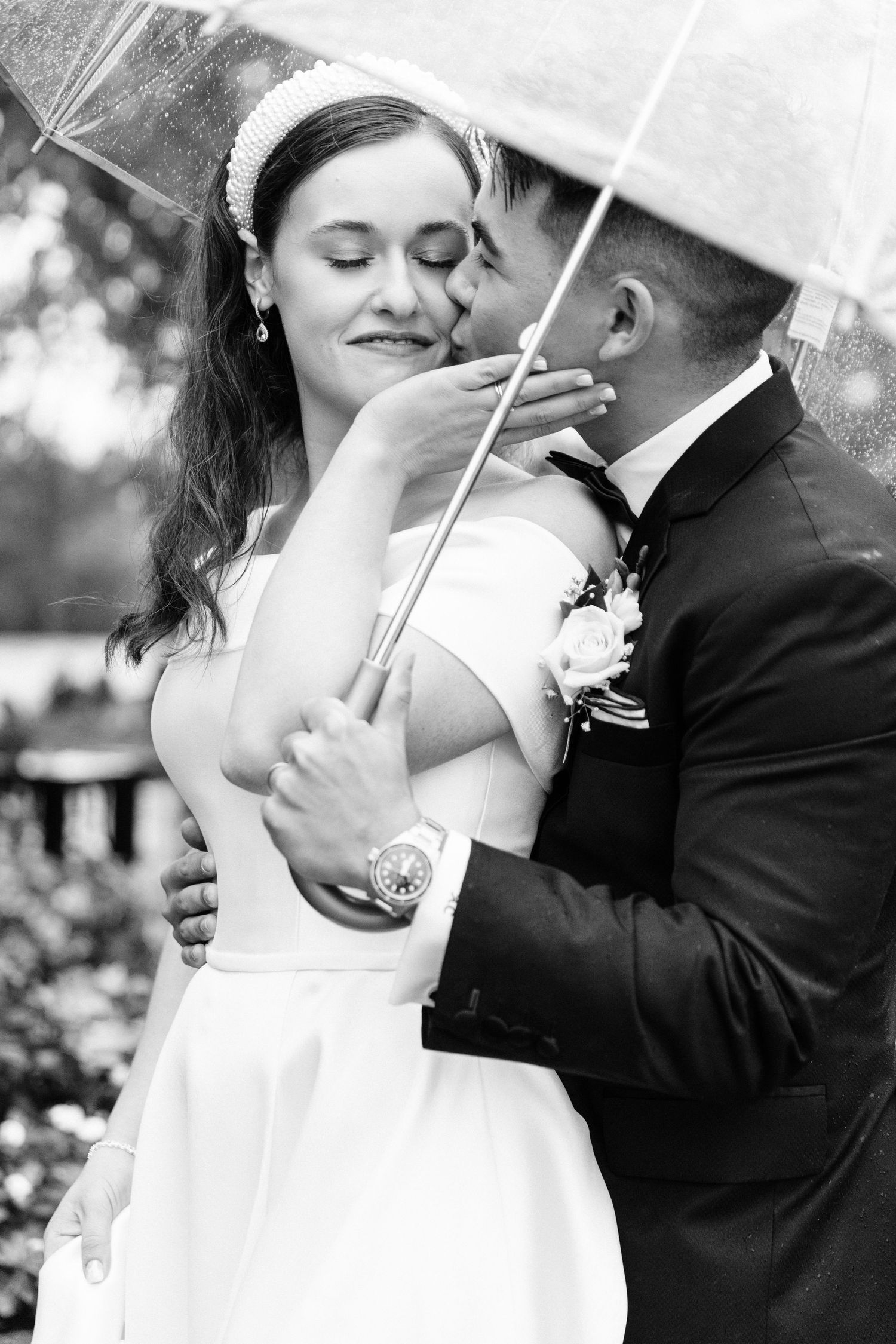 A romantic black and white wedding photo of a couple sharing an intimate moment under an umbrella.