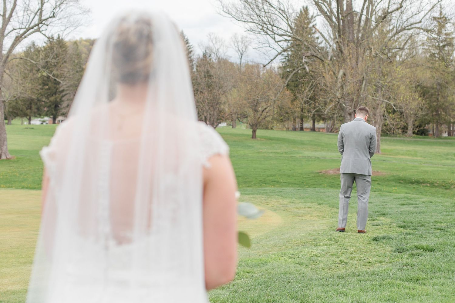 First look wedding moment captured on a scenic grassy hill with trees in background.
