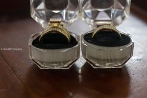 Two wedding rings displayed in clear jewelry boxes on wooden surface.