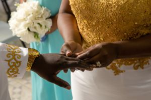 Close-up of hands exchanging rings during wedding ceremony with gold details.