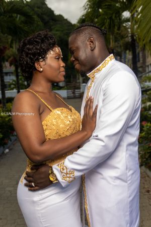 Elegant couple in white and gold formal wear pose in tropical garden setting.