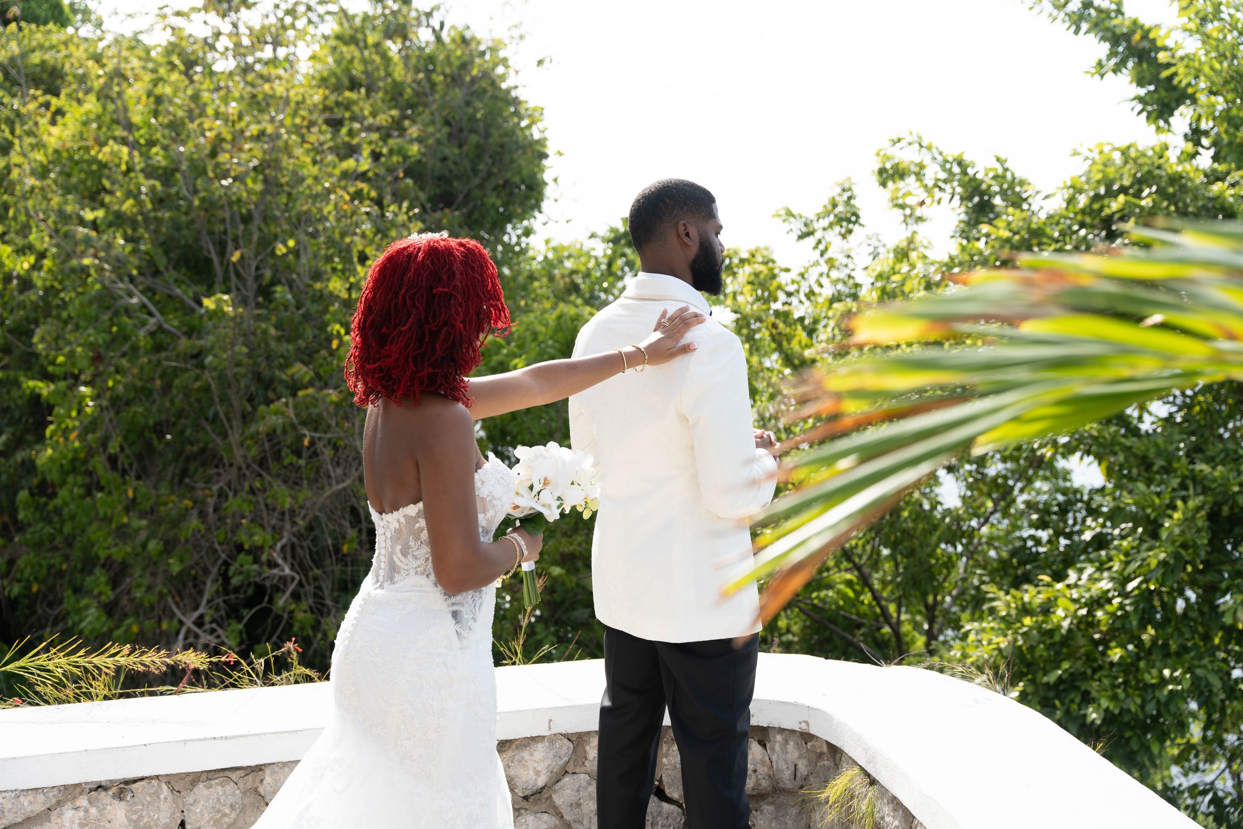 Wedding couple sharing a special moment on an oceanview terrace surrounded by tropical foliage.