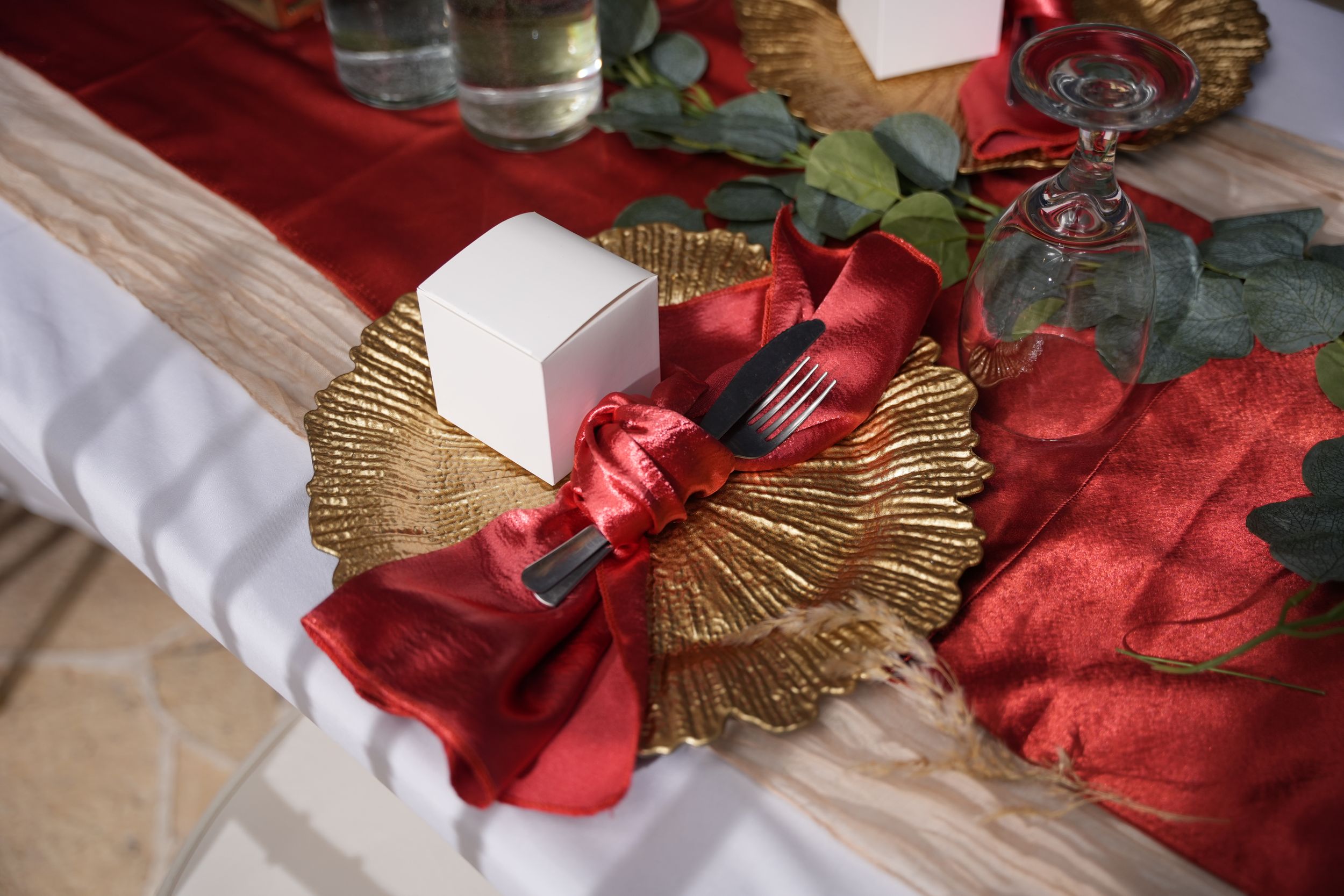 Decorative gold and red bow with wings on white and red table setting.