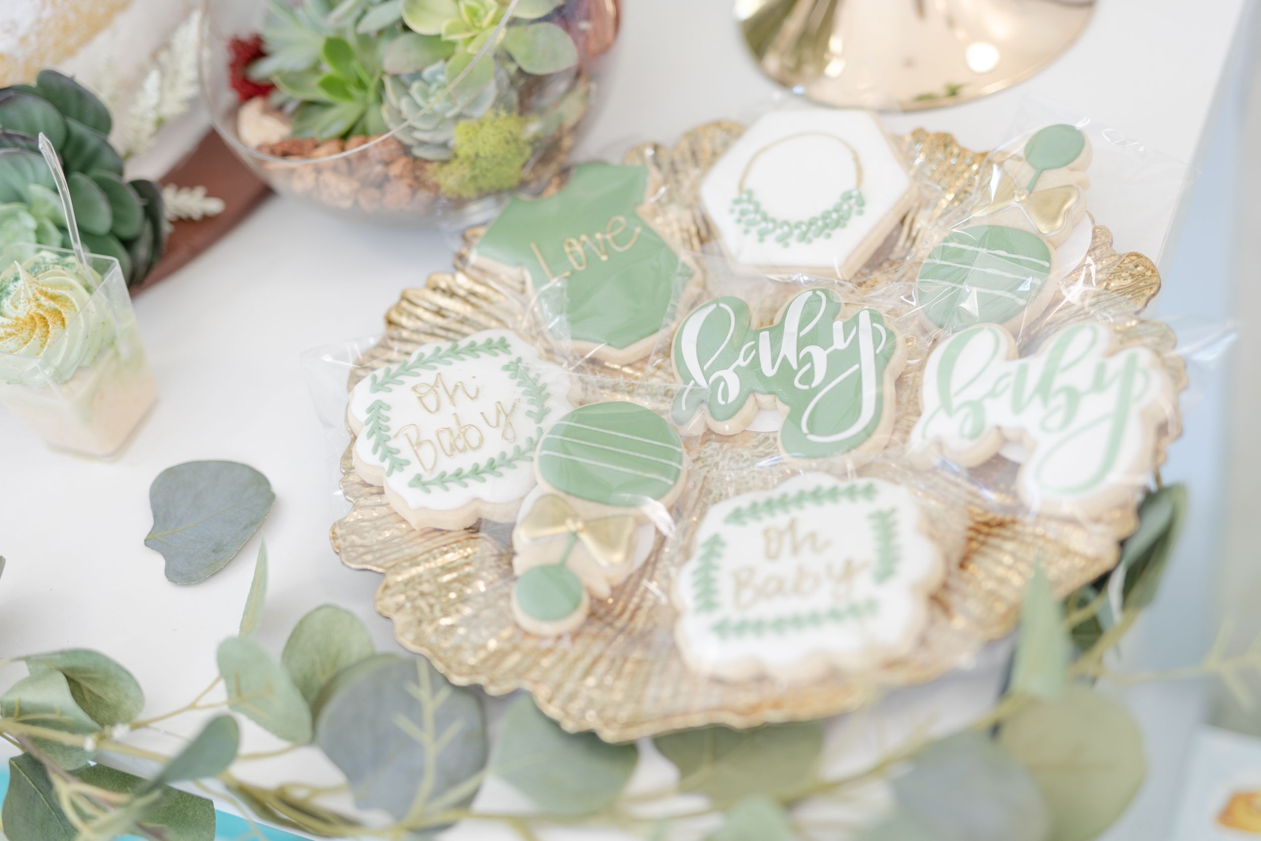 Decorative platter of baby shower cookies with mint green frosting and eucalyptus leaves.