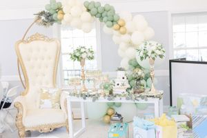 Luxurious baby shower setup with balloon arch, ornate throne chair, and pastel decorations.